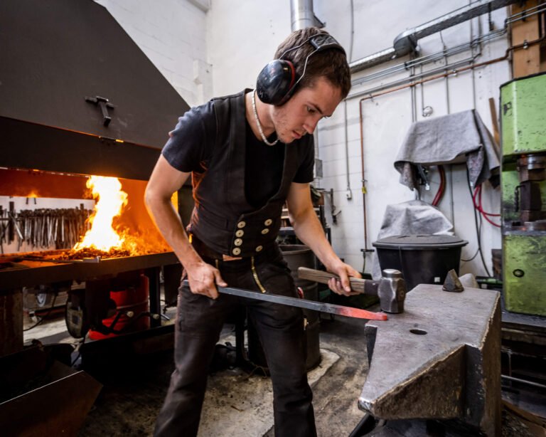 Lehrling Luke, der am Amboss glühendes Stahl bearbeitet in der Schmiede Lehmann in Hamburg.