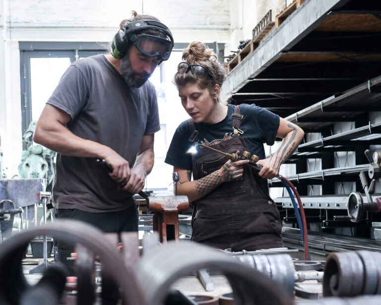 Ausbilder Micha und Lehrling Naima arbeiten in der Schmiede Lehmann in Hamburg zusammen.