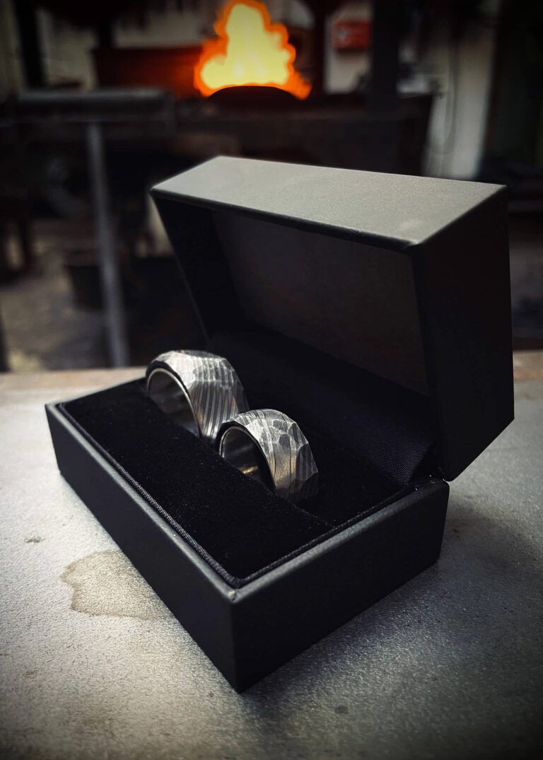 Handgeschmiedete Eheringe in einer schwarzen Ringschatulle vor dem Schmiedefeuer in der Schmiede Lehmann in Hamburg